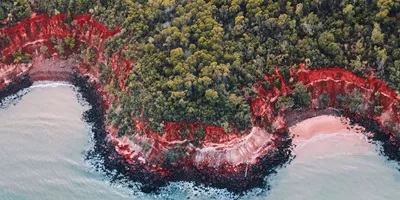 An aerial view of turquoise water, ochre red cliffs and verdant green trees on Tiwi Islands