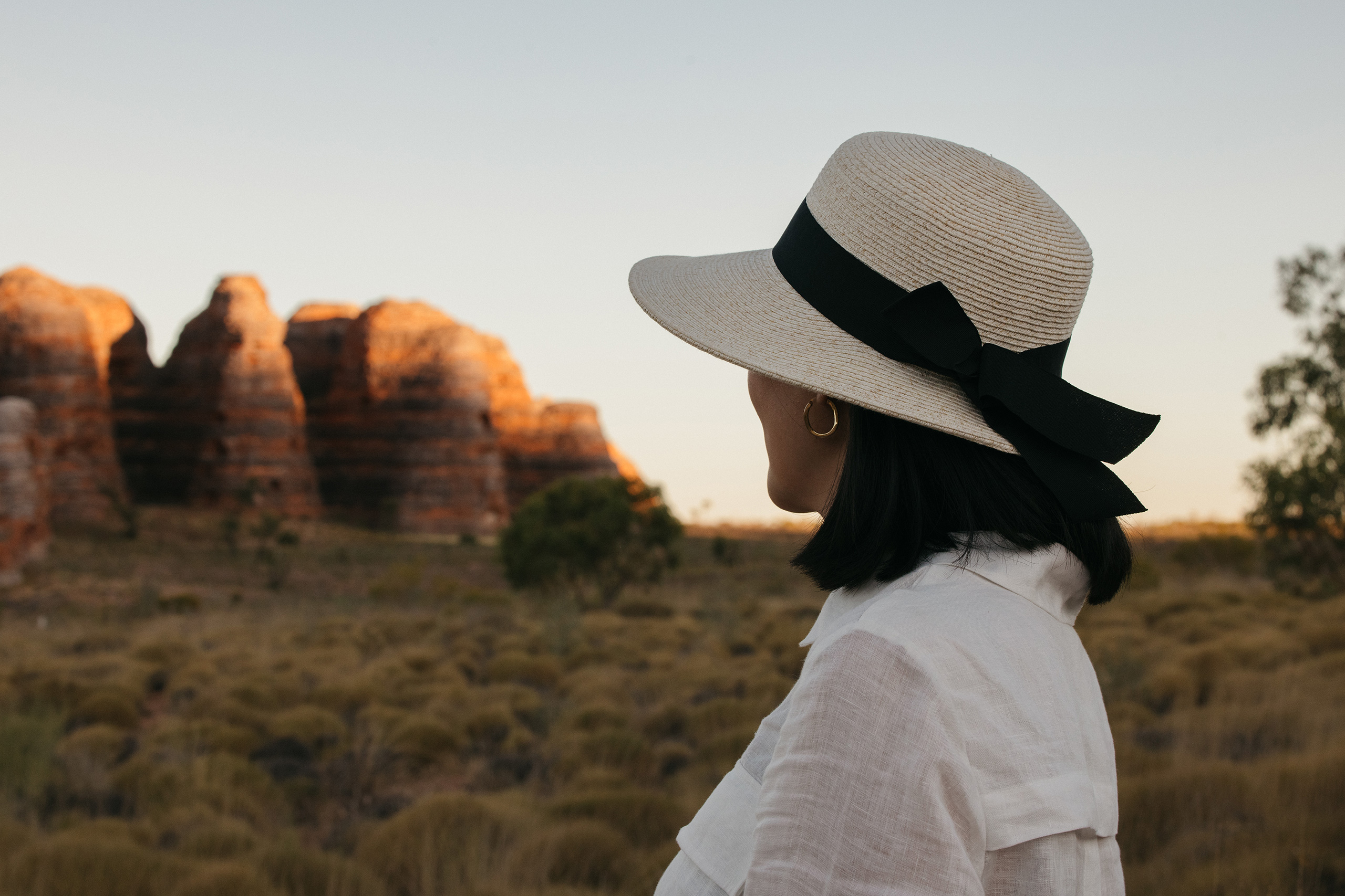 A woman in a cream wide brimmed hat with a black ribbon looking out over a beehive dome rock formation