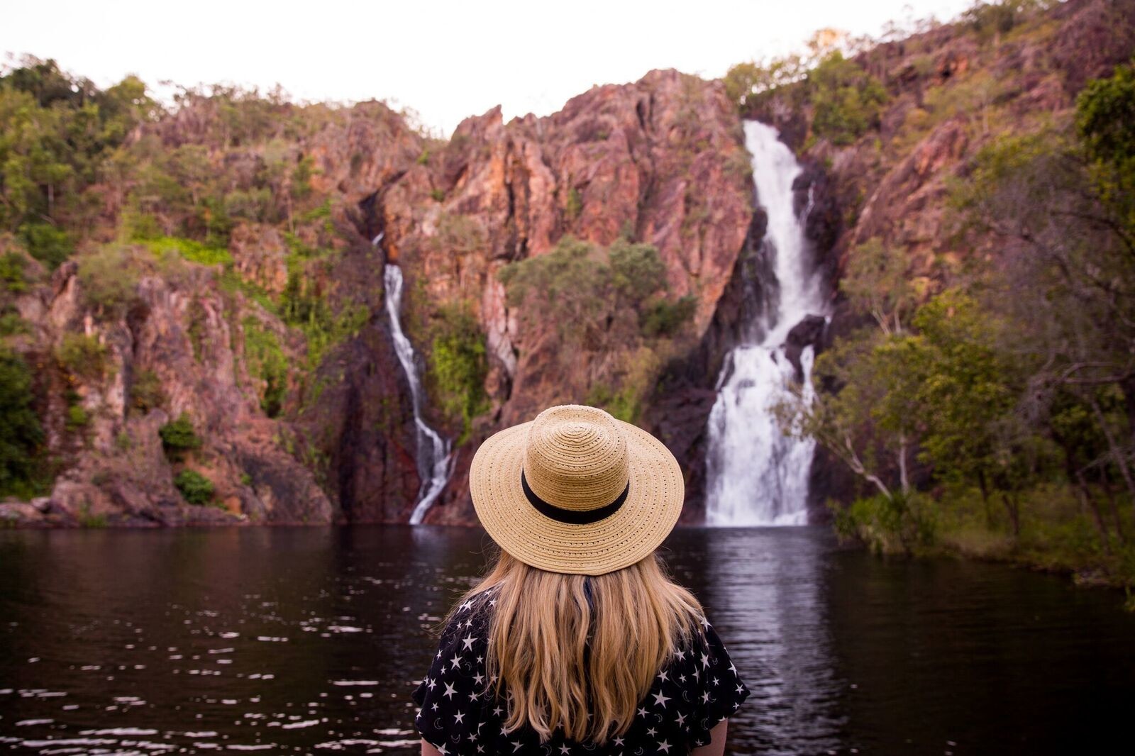 A woman with a hat standing in front of a waterfall