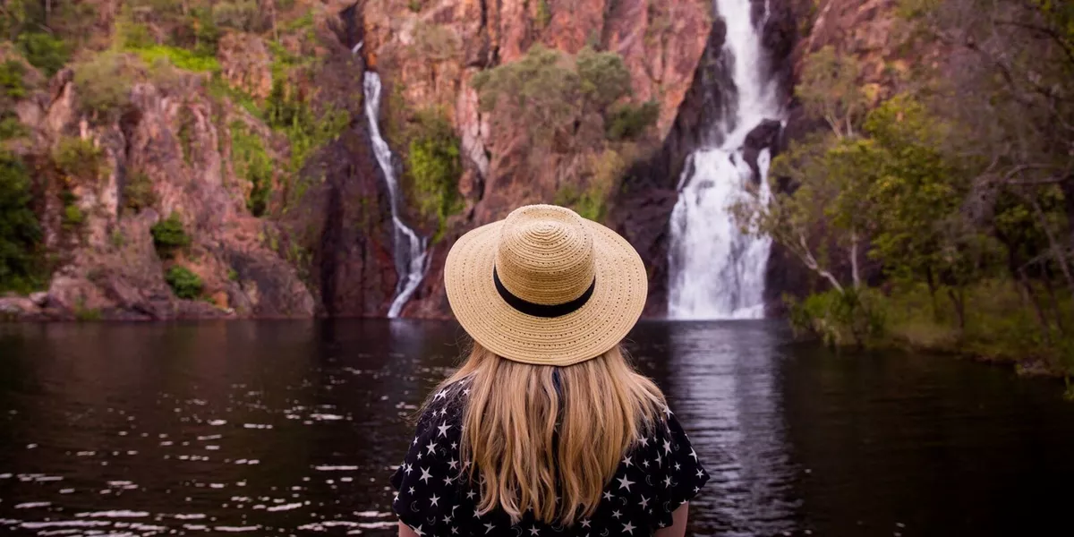 A woman with a hat standing in front of a waterfall