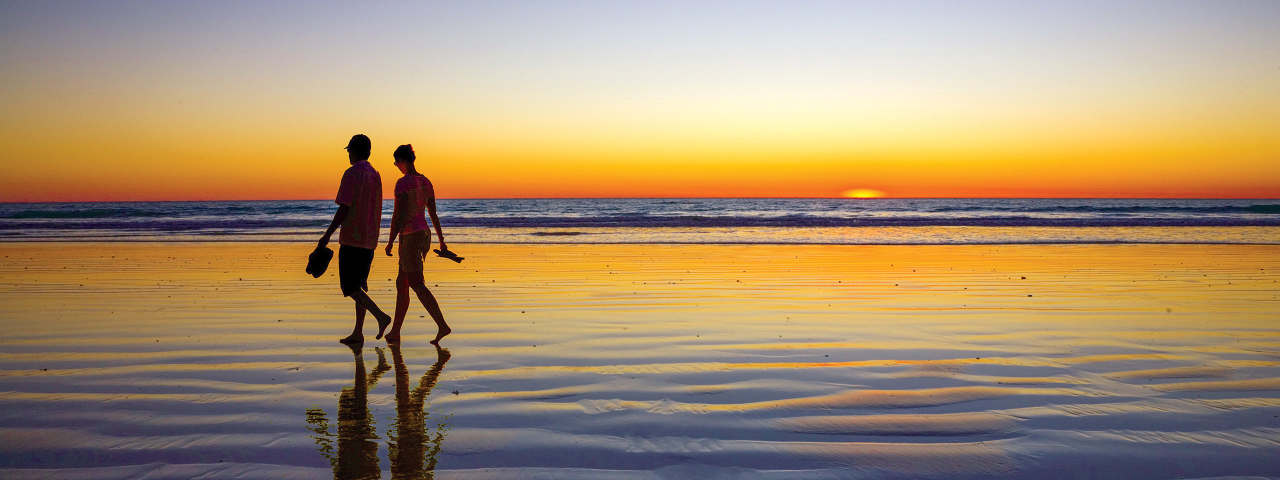 Couple walking by the shore of Broome City with sunset in the background