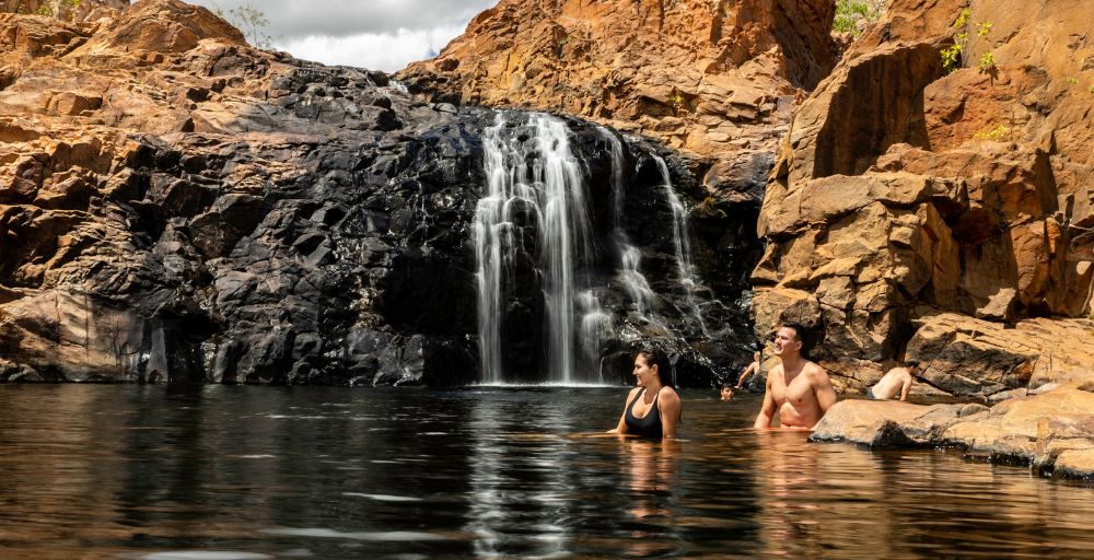 A couple of people in the water near waterfall