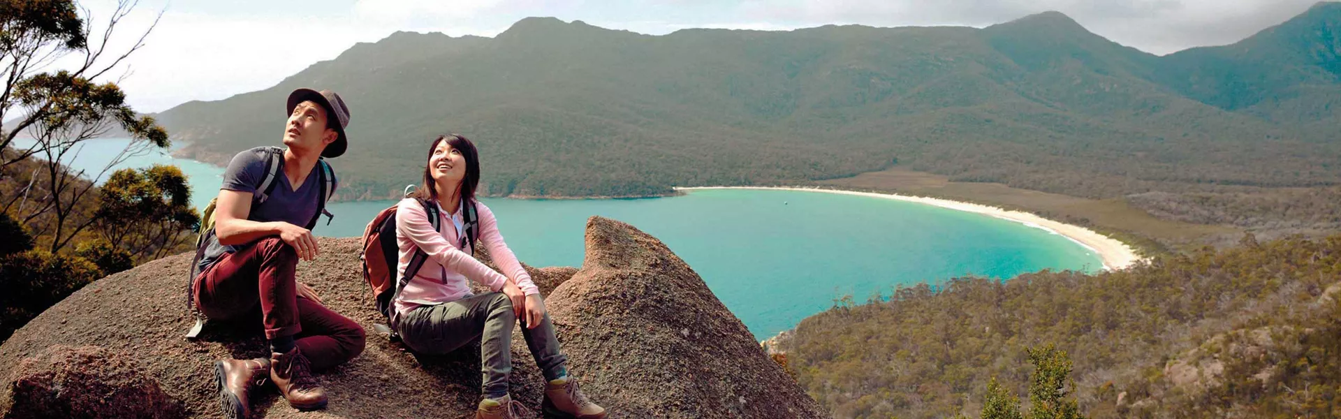 Tourists sitting on a rock enjoying the view of Wineglass Bay