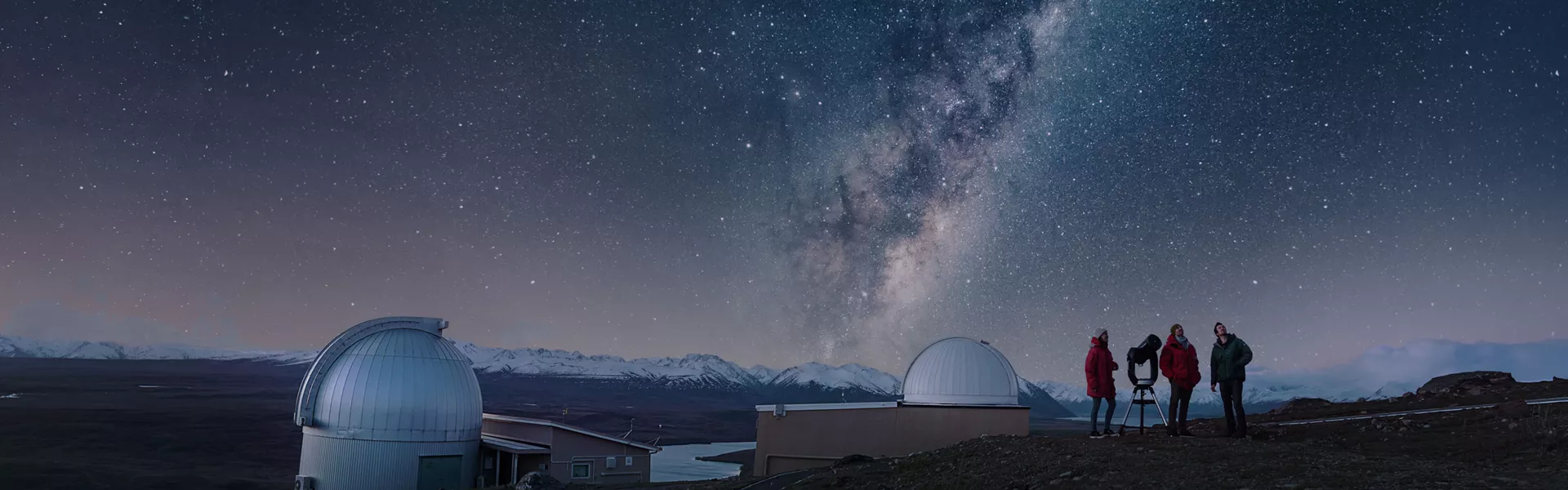 Three people standing on a hill looking at the stars