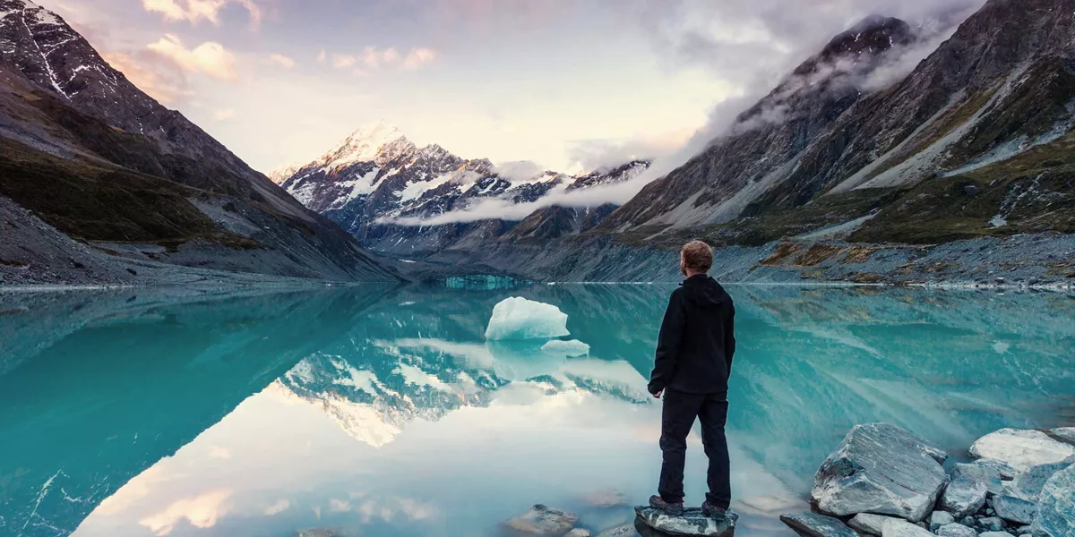 A man standing on a rock next to a body of water and view of the mountains