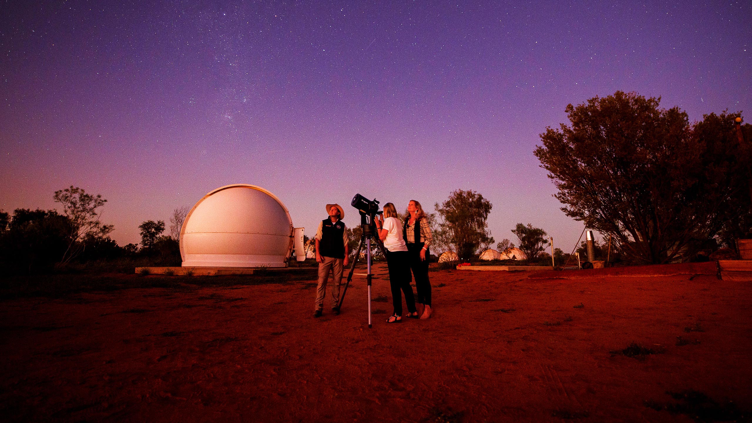 A group of people standing in front of a telescope and watching sky