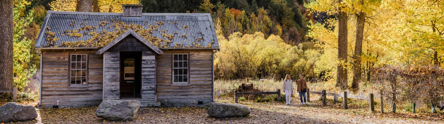 An old wooden cottage in the woods with two people walking