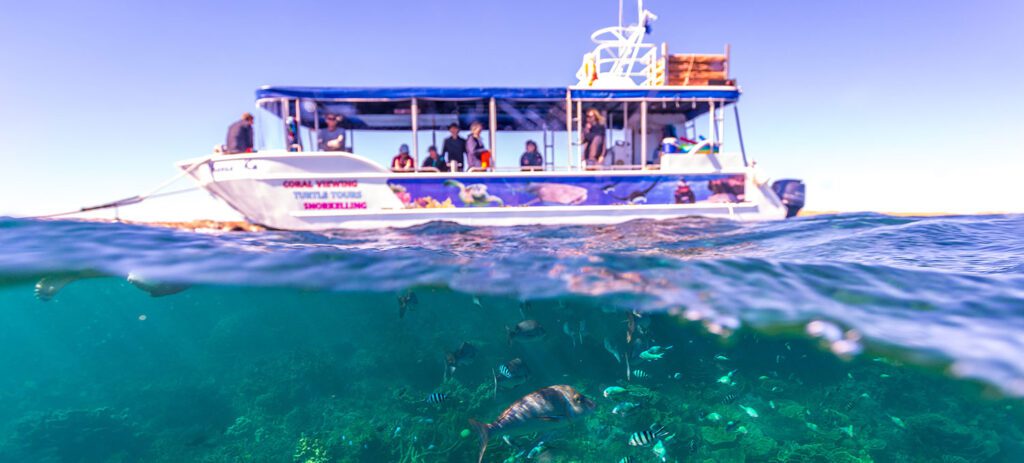 A glass-bottom boat floats above clear, shallow reef waters. 