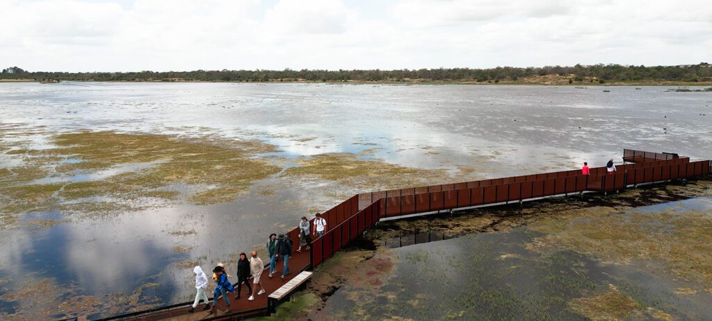 A boardwalk stretches over a wetland as visitors walk across the volcanic landscape of Budj Bim.