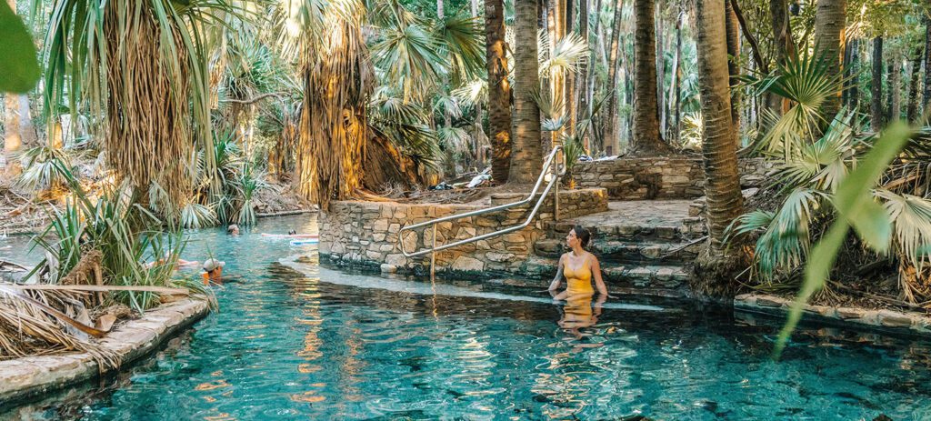 Woman relaxing in the crystal-clear thermal pools at Mataranka Springs in the Northern Territory, surrounded by tropical palm trees.