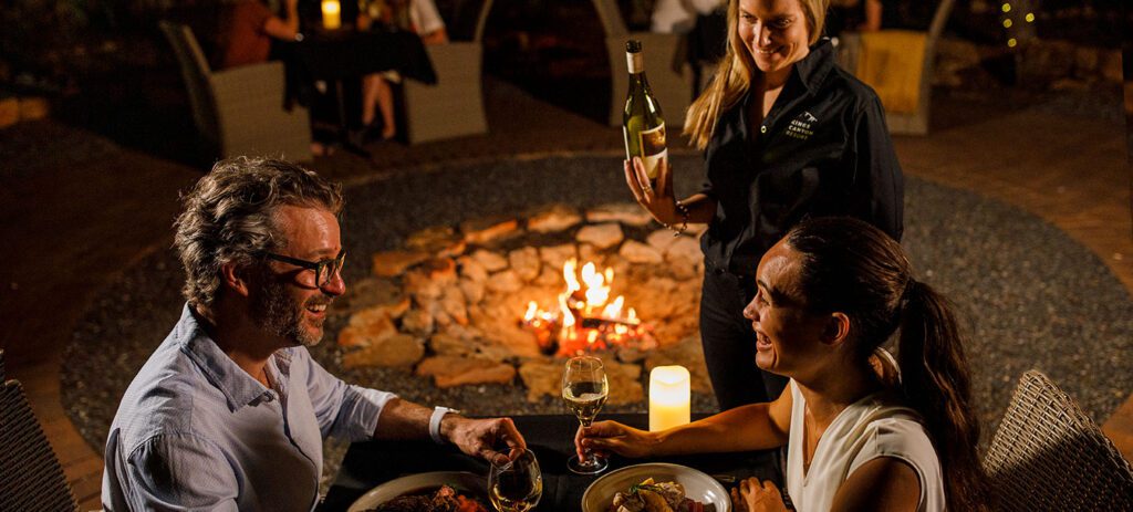 Two guests enjoying an Under a Desert Moon dinner in the Northern Territory as wine is poured at their table.