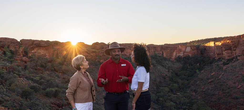 Two travellers talking beside their guide along the Kings Canyon Rim Walk, Northern Territory, at sunrise.