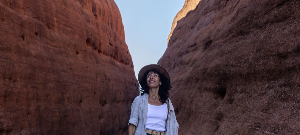 Woman standing in Walpa Gorge at Kata Tjuṯa looking up at towering rock walls.