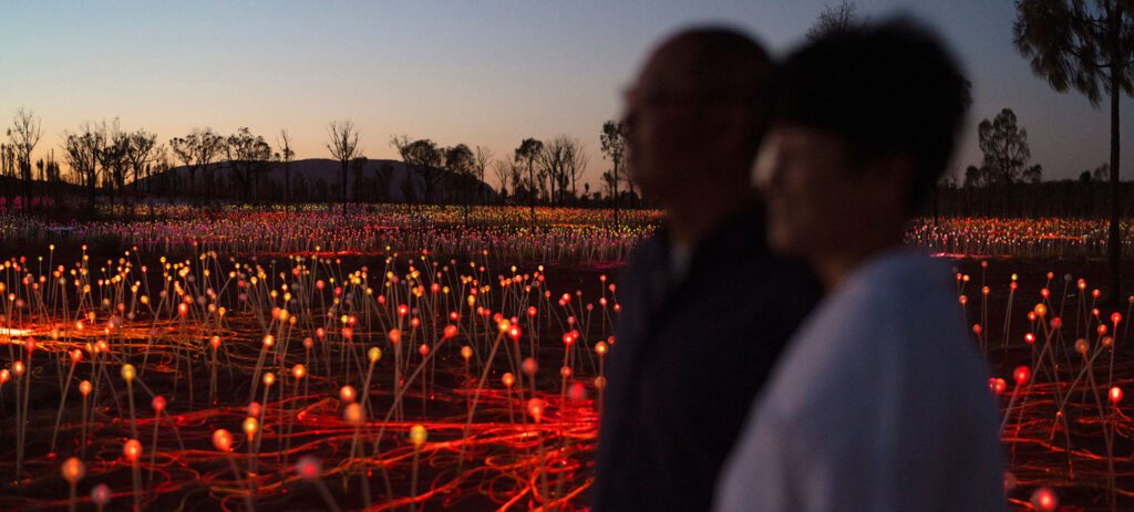 Two people in silhouette walking through a glowing Field of Light installation near Uluru
