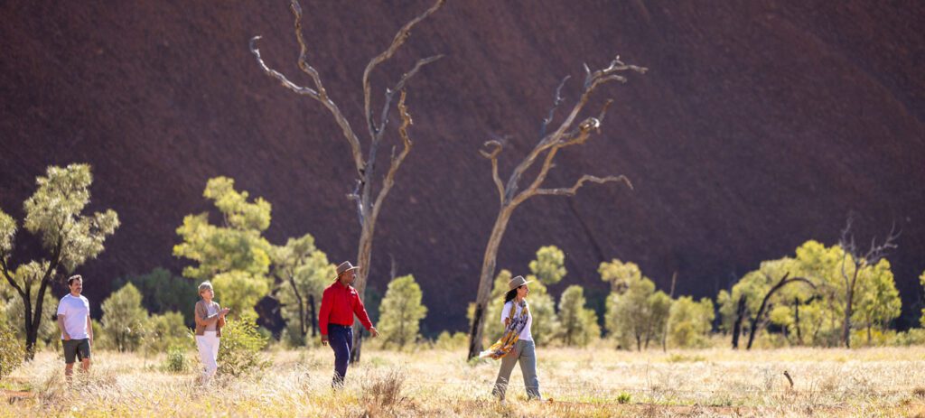 Travel Director and guests walking by foot at the base of Uluru