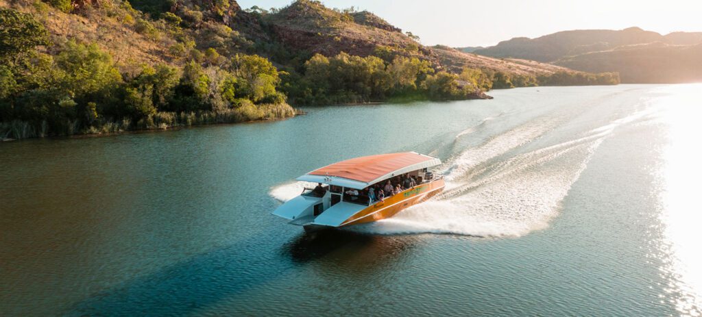 Aerial view of the Ord River in Western Australia with a boat creating a wake through blue water surrounded by greenery.