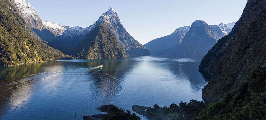 Misty fjord landscape in Fiordland National Park with steep green mountains and calm water under cloudy skies.