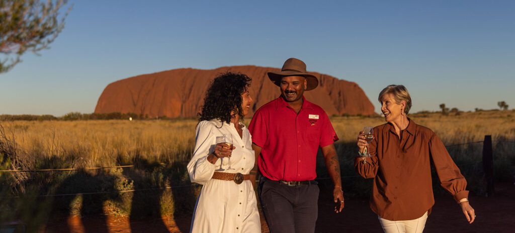 Travellers enjoying sunset drinks with a guide in front of Uluru in the Red Centre