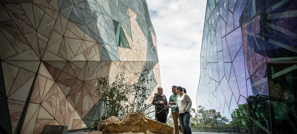 Two visitors exploring Federation Square with a First Nations cultural guide