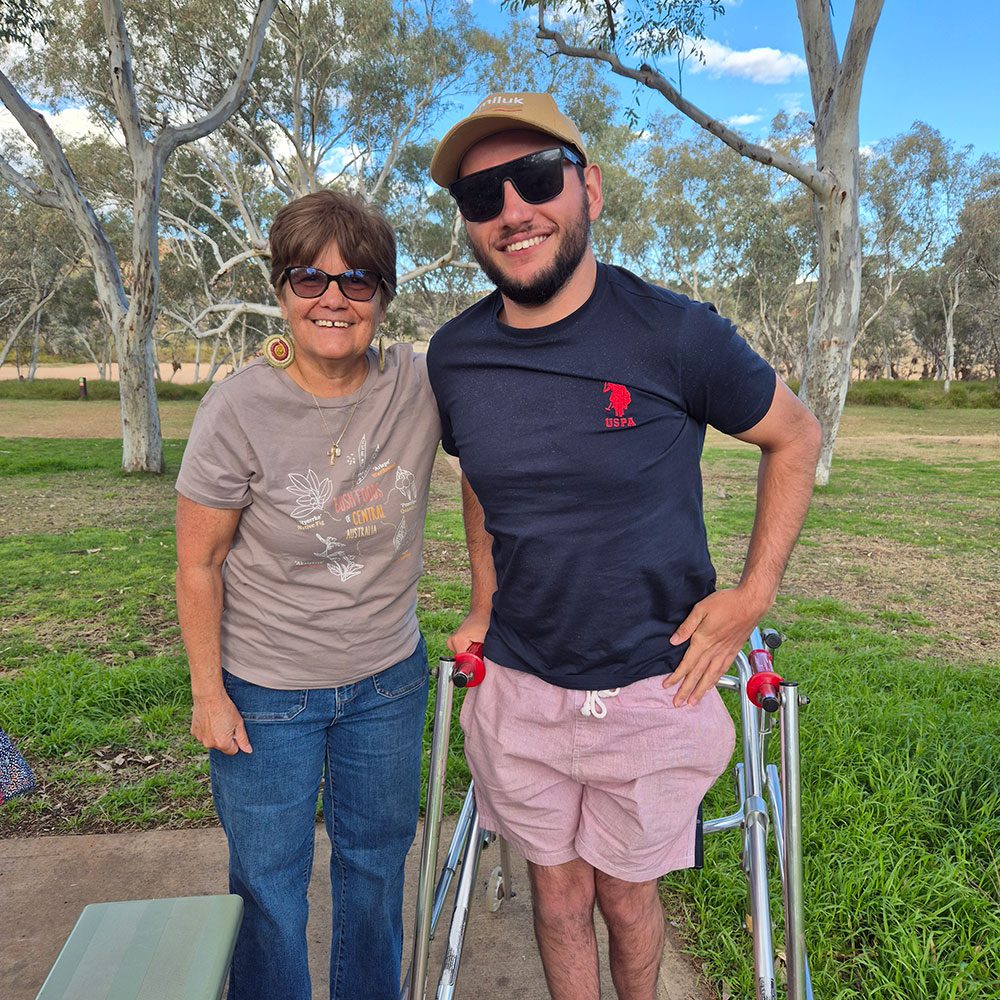 Smiling man using frame poses with a woman in sunglasses on a path surrounded by eucalyptus trees and grass.