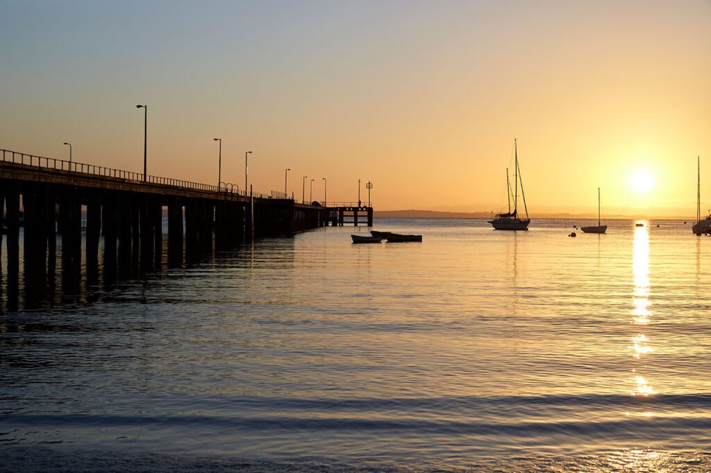 A long wooden pier at sunset with some sailboats on the water in Victoria, Australia