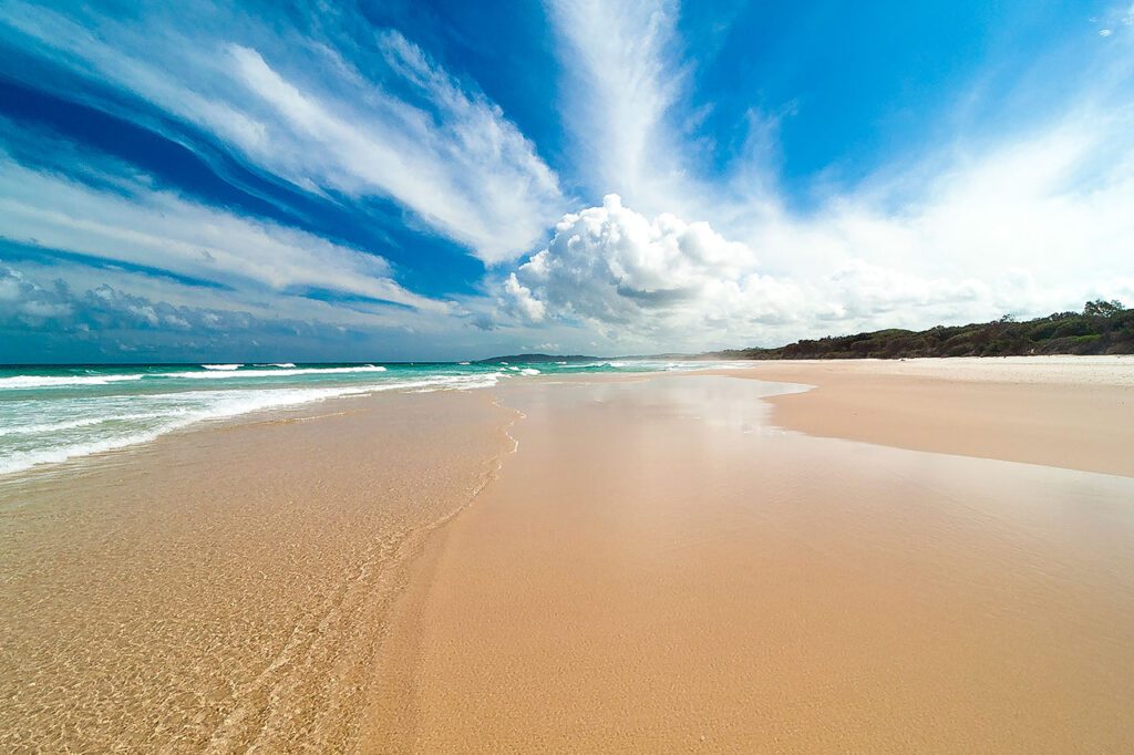 An empty stretch of pure sand at the edge of a turquoise ocean with small white-capped waves and blue sky in Queensland, Australia