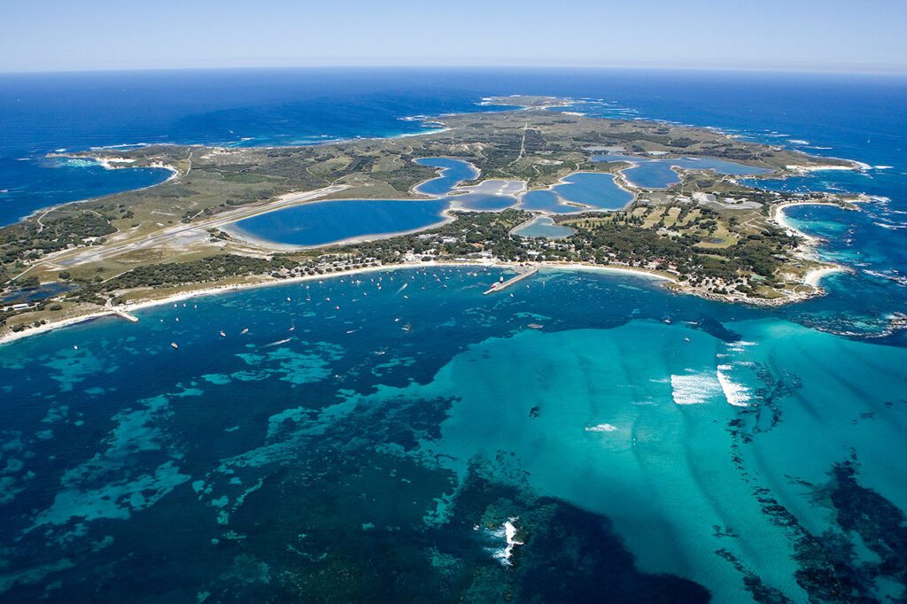 An aerial view of an island surrounded by a vibrant blue ocean with inland waterways and greenery on Rottnest Island, Western Australia