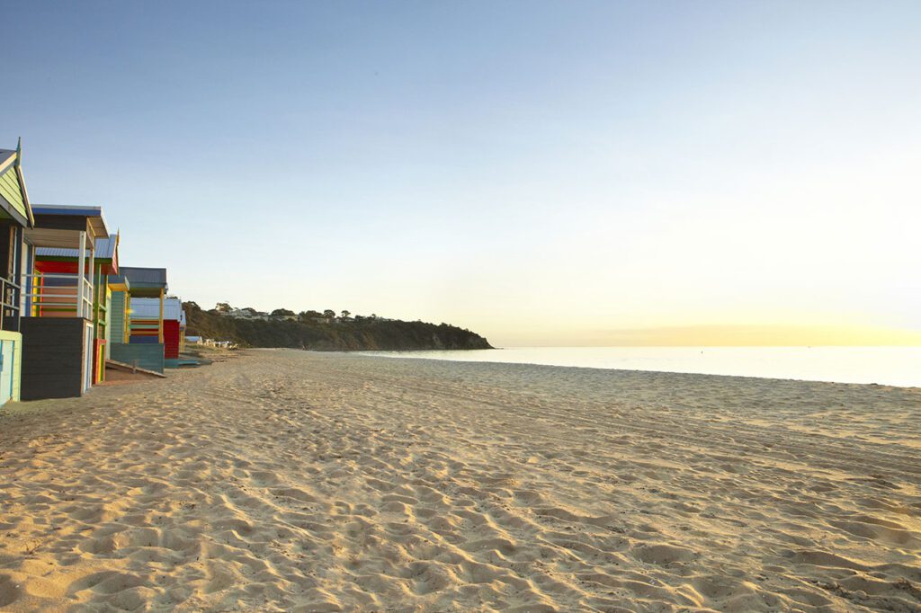 An empty sand beach with 5 colourful beach boxes lining the shore in Victoria, Australia