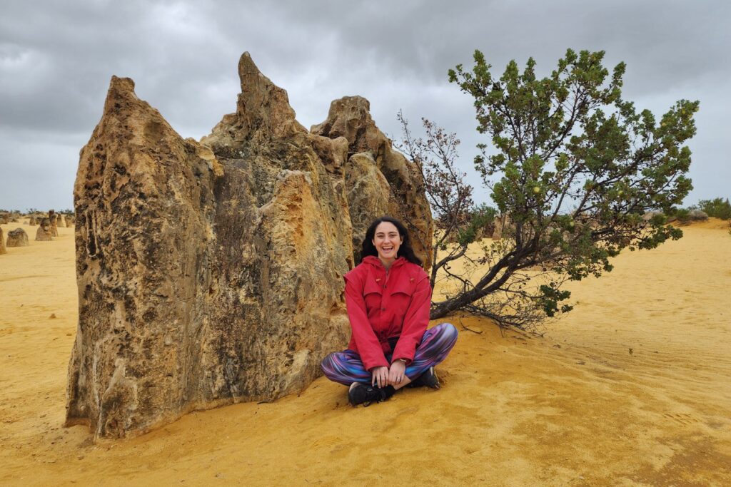 A girl in a red top sitting in front of a limestone formation in a desert landscape