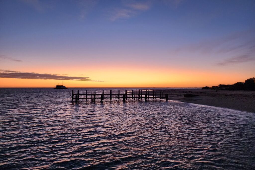 A wooden pier in the water at sunset