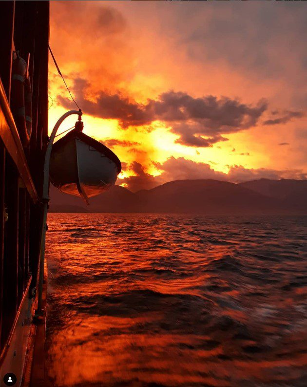 Side view of the historic TSS Earnslaw steamship docked in Queenstown harbour with golden sunset light illuminating the distant mountains.