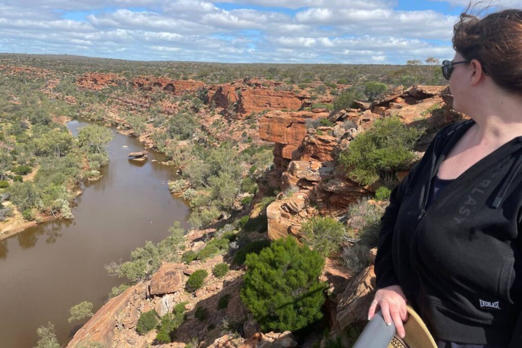 A girl standing at a lookout over a river and rocky background